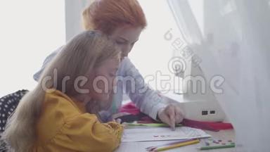 小女儿学习如何缝纫。 红头发的母亲向女孩展示如何选择衣服的纽扣