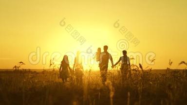 幸福家庭的观念.. 幸福的大家庭在夕阳下穿过田野。 父母和三个孩子走进来