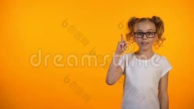 小天才女孩举起手指孤立在橙色背景下，有想法