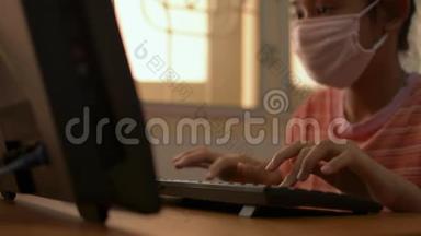 可爱的女孩戴着防护面罩，在COVID-19<strong>疫情</strong>爆发期间，在<strong>家</strong>里的桌子上使用电脑。