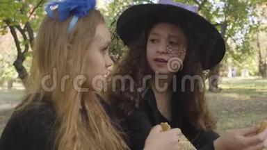 两个身着万圣节服装的可爱白人女孩在秋林里<strong>吃饼干</strong>的肖像。