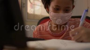 可爱的女孩戴着防护面具，在COVID-19疫情爆发期间，在家里用电脑写字。