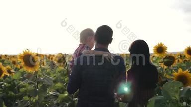 幸福的一家人和向日葵一起在田野里散步，一起享受生活，在户外携手并进。 他父亲抱着他