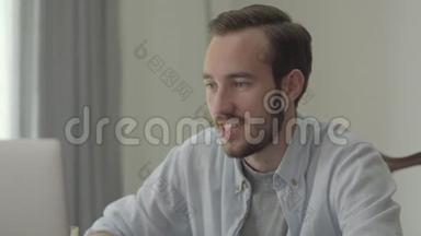 一个年轻英俊的男人坐在办公室的电脑前微笑点头的肖像。 上班族