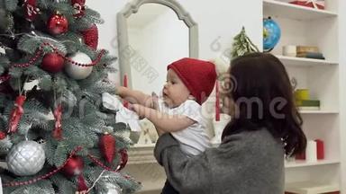 漂亮的微笑妈妈和可爱的婴儿站在<strong>装饰</strong>好的<strong>圣诞树</strong>孩子试图得到<strong>圣诞树</strong>