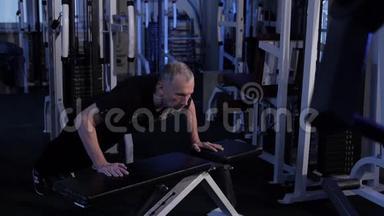 老人把自己从健身房的长凳上推下来。 复制空间.侧视图