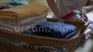 女人正在折叠衣服，放进一个木篮子里。 家庭主妇在卧室做家务活。