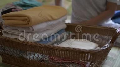女人正在折叠衣服，放进一个木篮子里。 家庭主妇在卧室做家务活。