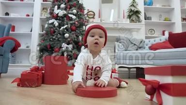 漂亮的<strong>小宝宝</strong>玩着圣诞盒子的<strong>红色</strong>盖子，坐在中间的木地板上