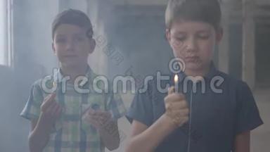 两个小男孩在一个烟雾弥漫的废弃房间里。 一个男孩拿着燃烧的火柴，第二个男孩拿着燃烧的打火机