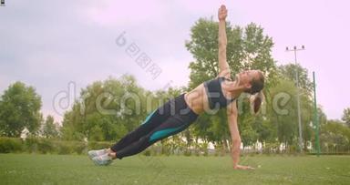 城市公园里，一个年轻漂亮的<strong>运动健身</strong>女孩正在做侧木板运动，伸展手臂