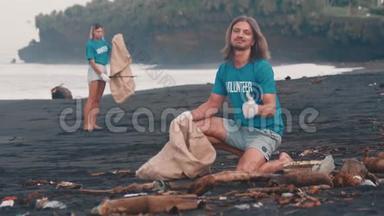 志愿者穿着蓝色t恤清理海滩上的垃圾，把垃圾叠在生态袋里