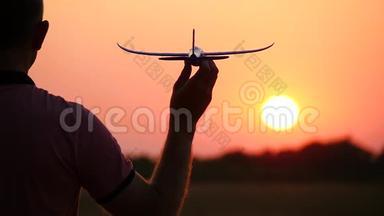 一个男人手里拿着一架模型飞机的剪影，在日落时站在太阳面前。 旅游概念