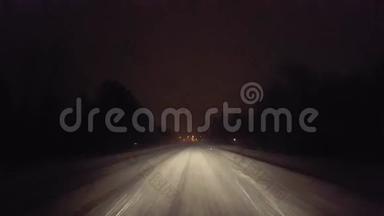 在暴风雪中开车，夜间在乡村道路上接近红绿灯。 司机视角POV接近城市灯光