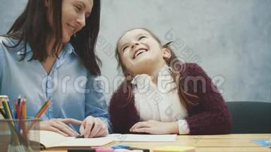 妈妈和女儿的灰色背景。 在这期间妈妈微笑着交流。 女儿写作业。 妈妈抱着她