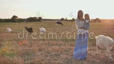 妈妈把一个一岁的女儿抱在怀里，她的背景是一片有山羊和奶牛的村庄。