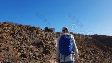 年轻女子背着背包在火山岛的荒山徒步旅行