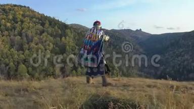 在秋天山景的背景下，一个老萨满带着手鼓的活力舞蹈。