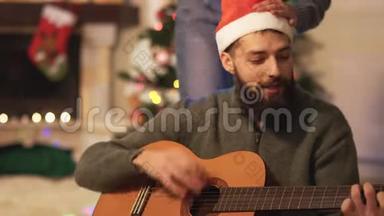 在现代房间里，坐在<strong>新年</strong>树附近的地板上弹吉他和唱<strong>歌</strong>的人。 脖子上戴着花环的女人