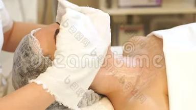 美容师用白餐巾纸在美容中心擦`女孩的脸。