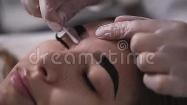 美容师用<strong>棉签</strong>擦拭妇女`眉毛，样式的形式。 修正眉毛。 特写侧视图