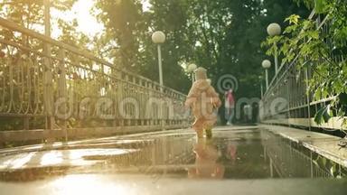 穿着橙色防水雨衣和橡胶<strong>雨靴</strong>的小女孩在水坑上向母亲走去，慢镜头