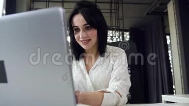 可爱的黑发年轻女商务<strong>小姐</strong>在笔记本电脑前工作，在<strong>办公室</strong>里微笑着