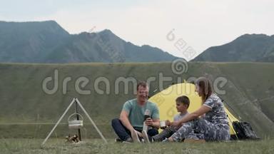 幸福的年轻家庭，有一个孩子在山上的帐篷前休息，喝热水瓶里的茶