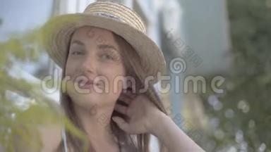 一位戴着草帽的漂亮年轻女人的特写脸，看着镜头，在户外快乐地微笑着。 情感，乡村