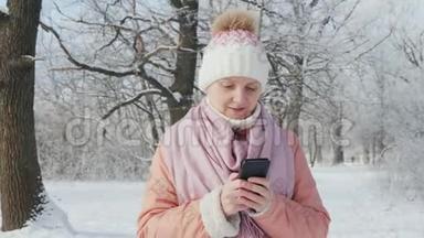 穿着粉红色夹克的女人喜欢在冬季公园散步。 使用手机