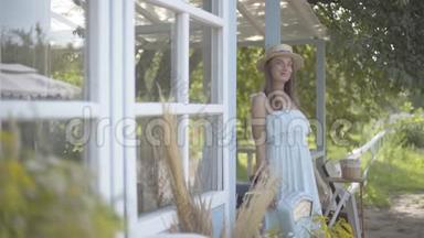 可爱的年轻微笑的女人，戴着草帽，穿着<strong>长长</strong>的白色连衣裙，远远望着小村庄的房子