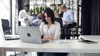 在公司背景下，现代办公室里，漂亮的黑发上班族在笔记本电脑上打字