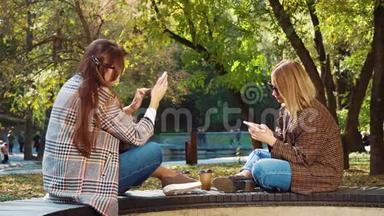 在秋<strong>季</strong>公园，时尚女孩面对面坐着，使用智能<strong>手机</strong>