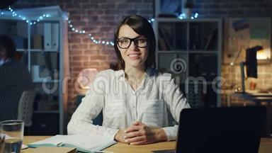 一位漂亮的商务小姐在办公室里，晚上坐在办公桌前微笑，动作缓慢