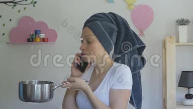 一个女人头上拿着毛巾，拿着一个金属平底锅从天花板上接水，在电话里说话。