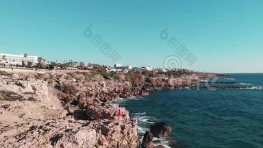 穿着红色衣服的女孩站在岩石悬崖上，双臂交叉。 白色强烈的海浪撞击海岸，形成白色泡沫和飞溅