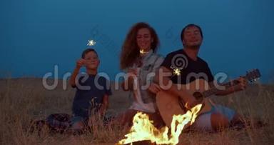 快乐的露营者<strong>全家</strong>围绕燃烧篝火，手持火花，微笑旅游休闲。