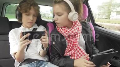 男孩和女孩带着耳机在汽车上玩平板电脑和智能手机，孩子们在汽车上使用设备。 兄弟和兄弟