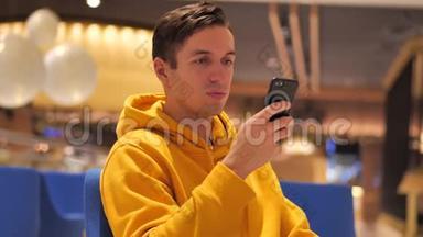 傍晚时分，穿着黄色连帽衫的年轻人在舒适的咖啡馆里使用智能<strong>手机</strong>。 沟通，商务，旅行，<strong>约会</strong>