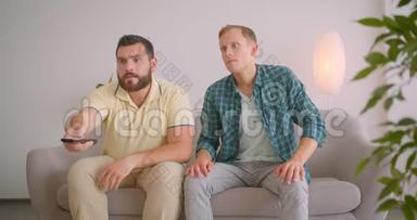 两个高加索人在<strong>电视</strong>上情绪激动地坐在家里的沙发上<strong>观看</strong>足球的特写照片