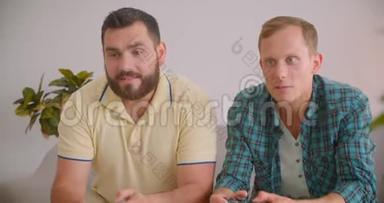 两个高加索兴奋的男人一起在舒适的室内沙发上玩电子游戏的特写镜头