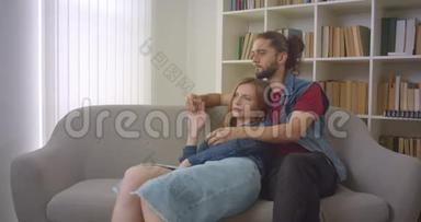 这张照片拍摄了年轻的白种人男女朋友坐在沙发上，温柔地拥抱在家里。