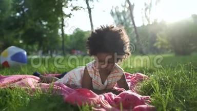 一个非裔美国女孩躺在公园里，躺在床上，用电话看动画片