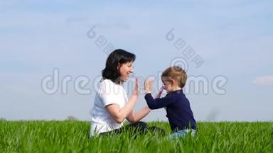 妈妈和小朋友坐在绿草上玩耍，互相拍打`的手。 家庭幸福、<strong>关爱</strong>的理念