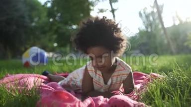 一个非裔美国女孩躺在公园里，躺在床上，用<strong>电话</strong>看<strong>动画</strong>片