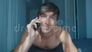 快乐微笑的男人早上在家里的床上谈论<strong>手机</strong>。 电信生活方式。 <strong>手机通话</strong>