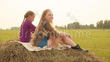 两个十几岁的女孩坐在村里的收割场上的干草堆上。 无忧无虑的少女在干草堆上放松