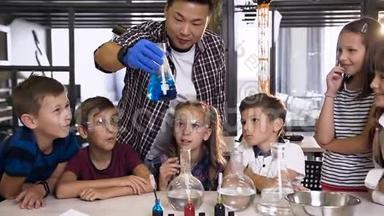 男韩语老师在课堂上展示青年学生化学实验.. 玻璃瓶中蓝色化学反应