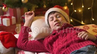 圣诞老人帮手男孩睡觉和等待圣诞老人，躺在装饰的圣诞树附近，灯光-圣诞快乐和节日快乐！