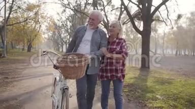 在雾蒙蒙的公园里，一对快乐的白人夫妇骑着自行车沿着小巷散步。 退休的成熟家庭开支